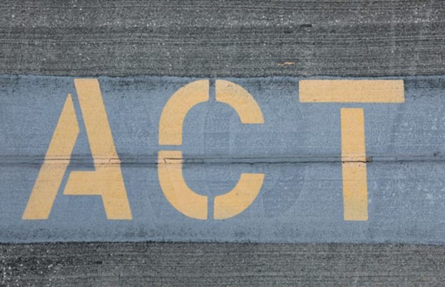 Close-up of the word 'ACT' painted in yellow on a concrete surface, emphasizing action and awareness.